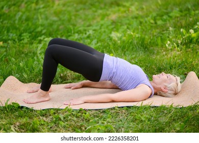 Athletic attractive middle aged woman practicing yoga doing yoga in nature in bridge pose. Glute bridge pose.The concept of stretching, pilates, doing sports in nature. - Powered by Shutterstock