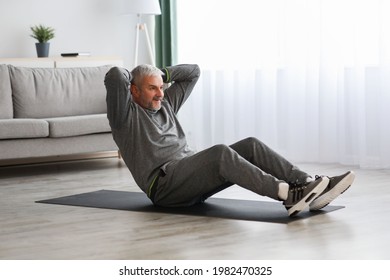 Athletic Bearded Senior Man In Grey Sportswear Doing Exercises For Abs At Home, Sitting On Fitness Mat And Crunching, Copy Space. Healthy Lifestyle, Sport On Self-isolation For Older People