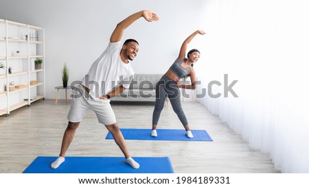 Athletic black couple bending aside, doing exercises at home, banner design with free space. African American guy and his lovely girlfriend having domestic training, working out together indoors