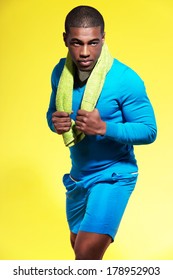 Athletic Black Man In Sportswear Fashion. Runner With Towel. Intense Colors. Studio Shot Against Yellow.