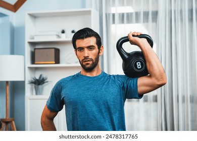 Athletic body and active sporty man lifting kettlebell weight for effective targeting muscle gain at gaiety home as concept of healthy fit body home workout lifestyle. - Powered by Shutterstock