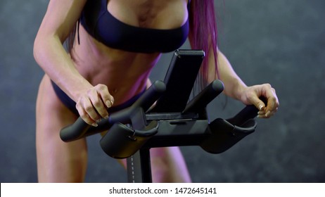 the athletic body of a girl with long purple hair, in a topic and in panties, which is engaged on a stationary bike. - Powered by Shutterstock