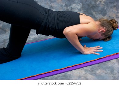 An athletic brown haired woman is doing yoga exercise Sunbird posture on yoga mat in studio with mottled background.