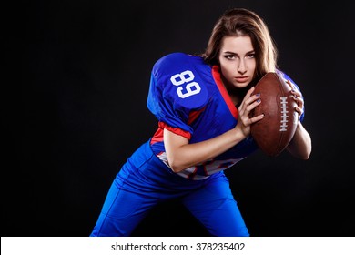 athletic brunette posing as american football girl on black background. Beautiful young woman wearing American football top holding ball. studio photo of american football woman