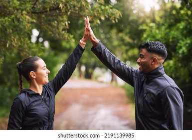 Athletic couple high five while exercising in a park or forest, celebrating and winning before a run. Fit boyfriend and girlfriend bonding while keeping fit and healthy. Fun lovers being active