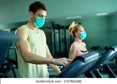 Athletic Couple Running On Treadmill While Wearing Protective Face Masks At Health Club. Focus Is On Man. 