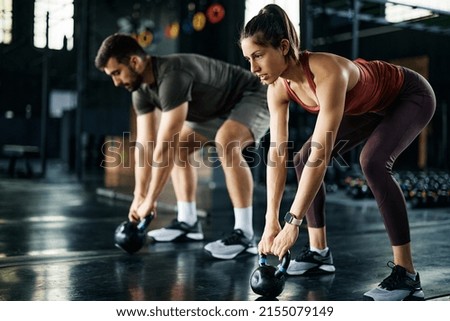 Athletic couple using kettle bells during cross training in a gym. 