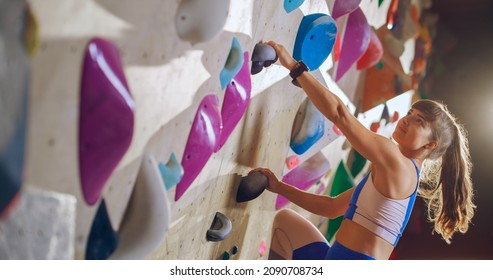 Athletic Female Rock Climber Practicing Solo Climbing On Bouldering Wall In Gym. Female Exercising At Indoor Fitness Facility, Doing Extreme Sport For Her Healthy Lifestyle Training. Close Up Portrait