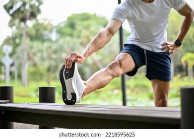 Athletic fit Asian man in sportswear is stretching his leg on a bench, warming up before running or cooling down after a long run. cropped image - Powered by Shutterstock