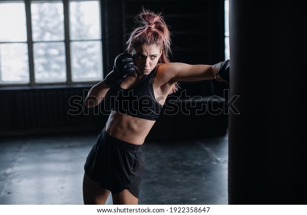 Athletic\
fit female boxer exercising punches with boxing bag in gym during\
kickboxing and self defense intensive\
workout