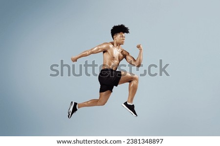 Athletic fit man sprinting and leaping forward with arms tensed, having sport training on soft blue background. Guy having workout, running in mid air. Full length shot with copy space, side view