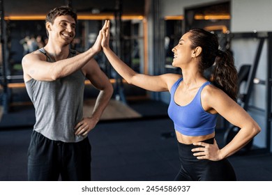 Athletic fitness lady and coach man give high five during training in dark gym interior, smiling at each other - Powered by Shutterstock
