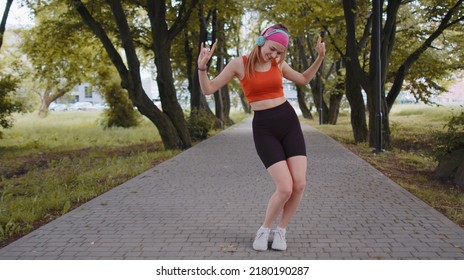 Athletic fitness sport runner girl training exercise, listening music on headphones dancing to camera having fun. Workout cardio in park. Young woman jogger enjoying funny dance. Active sportswoman - Shutterstock ID 2180190287