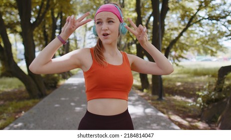 Athletic fitness sport runner girl training exercise, listening music on headphones dancing to camera having fun. Workout cardio in park. Young woman jogger enjoying funny dance. Active sportswoman - Shutterstock ID 2184814047