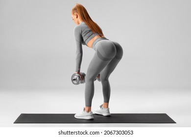 Athletic Girl Doing Deadlift Exercise For Glutes On Gray Background. Fitness Woman Working Out With Dumbbells