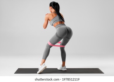 Athletic girl doing exercise for glute with resistance band on gray background. Fitness woman working out