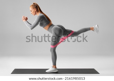 Athletic girl doing exercise for glutes with resistance band on gray background. Fitness woman working out
