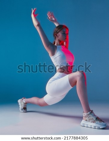 Athletic girl doing lunges exercises with raised hands in pink neon light. Long exposure. Fitness workout, wellness