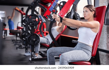 Athletic girl doing strength training in gym, exercising upper body muscles on shoulder press machine - Powered by Shutterstock