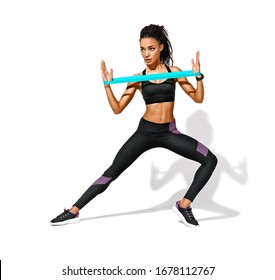 Athletic girl performs exercises using resistance band. Photo of african american girl in black sportswear on white background. Strength and motivation