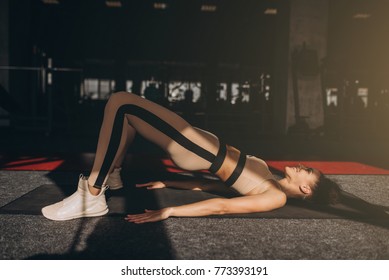 Athletic Girl In Rose Sportswear Does Stretching Exercise On The Track Indoors. She Holds Her Feet On The Toes And Raises Her Pelvis While Relies On The Hands And Shoulders.