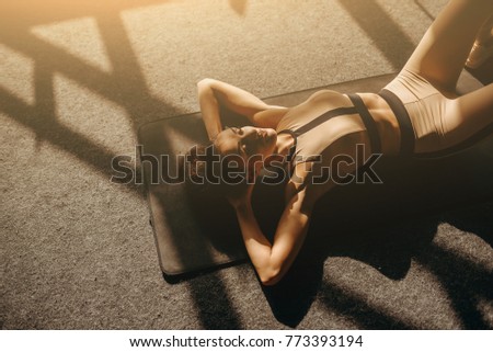Athletic girl in rose sportswear does stretching exercise on the track indoors. She holds her feet on the toes and raises her pelvis while relies on the hands and shoulders.