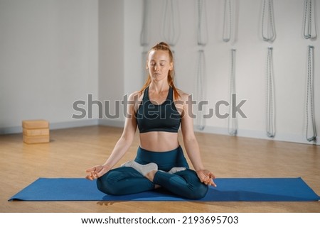 Athletic girl sitting on a yoga mat in a lotus position and looking at camera