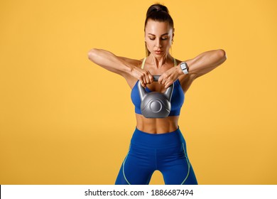 Athletic girl working out with kettlebell on orange background. Fitness woman doing exercise for delt