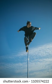 Athletic guy make acrobatic elements on pylon. Sexy macho man fly on blue sky background. Young man dancing on pylon. Strong man dancer workout on pole. Pole dance sport. Training to become the best