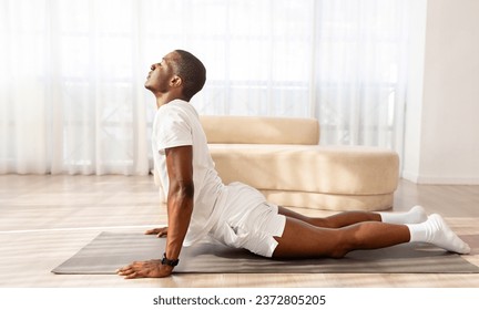 Athletic handsome young black man in sportswear stretching on yoga mat, doing morning workout at home, practicing yoga, copy space, full length candid shot, side view. Healthy lifestyle, sport - Powered by Shutterstock