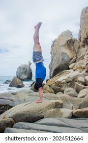 An athletic Hispanic man doing a headstand on a rock against an ocean view