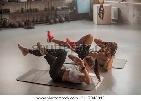 Athletic instructor and young lady doing abs exercises in a sports club