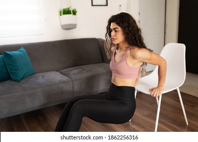 Athletic latin woman in her 20s working out her arms with tricep dips exercises. Good-looking woman using a chair for her home workout