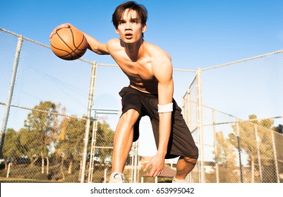 Athletic male basketball player in action outdoors. Boy dribbling the ball at the streetball court.  - Powered by Shutterstock