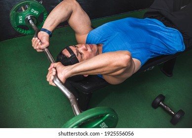 An athletic male does a set of lying tricep extensions, also known as skull crushers. An isolation exercise at the gym.