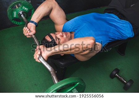 An athletic male does a set of lying tricep extensions, also known as skull crushers. An isolation exercise at the gym.