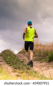 Athletic Male Runner Running Uphill On Dirt Road. Low Angle Back View.