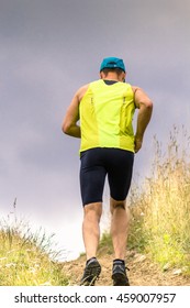 Athletic Male Runner Running Uphill On Dirt Road. Low Angle Back View.