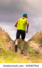 Athletic Male Runner Running Uphill On Dirt Road. Low Angle Back View.