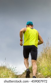 Athletic Male Runner Running Uphill On Dirt Road. Low Angle Back View.