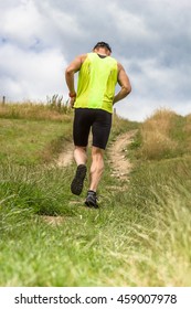 Athletic Male Runner Running Uphill On Dirt Road. Low Angle Back View.