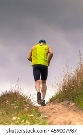 Athletic Male Runner Running Uphill On Dirt Road. Low Angle Back View.