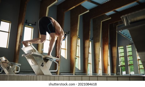 Athletic Male Swimmer Standing On A Starting Block, Ready To Jump Into Swimming Pool. Determined Professional Athlete Training For The Championship. Cinematic Light. Semi Side View Shot