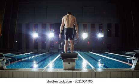 Athletic Male Swimmer Stands On A Starting Block, Ready To Dive Into Swimming Pool. Determined Professional Muscular Athlete Prepares For Championship. Cinematic Light