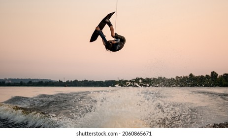 athletic male wakeboarder masterfully jumping and flips on wakeboard over splashing wave. Wakeboarding and water sports activity.
