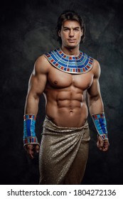 Athletic man in ancient egyptian costume posing in the studio with graphite walls