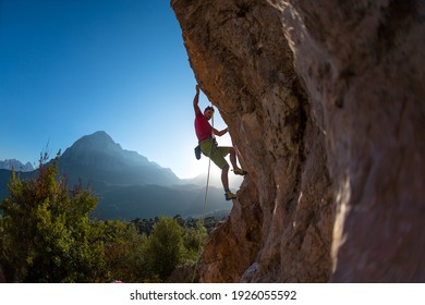 Athletic man climbs an overhanging rock with rope, lead climbing. silhouette of a rock climber on a mountain background. outdoor sports and recreation