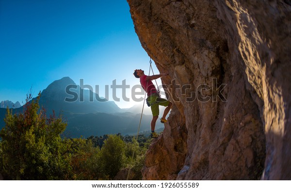 Athletic man climbs an overhanging rock with\
rope, lead climbing. silhouette of a rock climber on a mountain\
background. outdoor sports and\
recreation