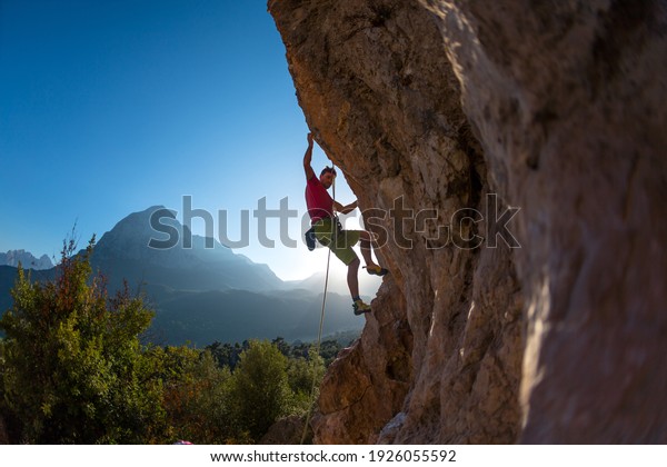 Athletic man climbs an overhanging rock with\
rope, lead climbing. silhouette of a rock climber on a mountain\
background. outdoor sports and\
recreation