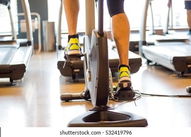 Athletic Man Cycling On Stationary Bike In Gym. Focus On Leg.